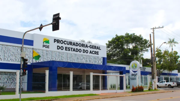 PGE-AC lança concurso com salário de R$ 25,9 mil para Procurador 2 Fachada da Procuradoria-Geral do Estado do Acre com prédio moderno em azul e branco, exibindo o letreiro oficial do órgão e bandeiras posicionadas na entrada. Foto: Divulgação/PGE-AC