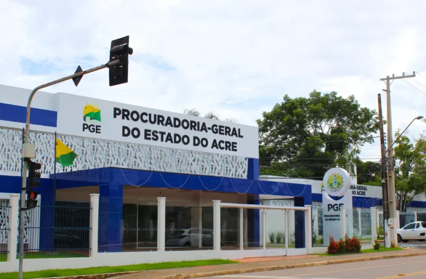 Fachada da Procuradoria-Geral do Estado do Acre com prédio moderno em azul e branco, exibindo o letreiro oficial do órgão e bandeiras posicionadas na entrada. Foto: Divulgação/PGE-AC