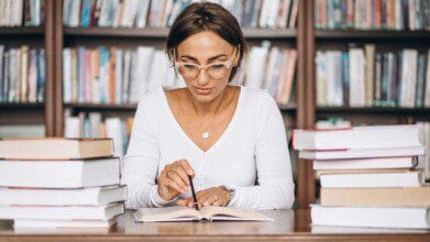 Mulher estudando em uma biblioteca com livros empilhados sobre a mesa. Foto: senivpetro /Freepik