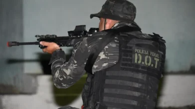 Policial penal do D.O.T. com uniforme camuflado e colete tático apontando uma arma durante treinamento ou operação. Foto: Divulgação/PPES