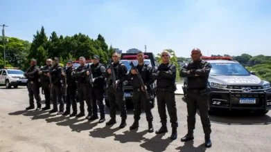 PPSP abre concurso c/ 1100 vagas imediatas de Policial Penal 3 Grupo de policiais penais fardados em formação, armados, posando em frente a viaturas oficiais em área externa. Foto: Divulgação/Mônica Andrade/Governo do Estado de SP