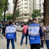 Servidores do Procon/RJ com coletes azuis realizam atendimento ao público em calçada do Centro do Rio de Janeiro, com prédios e pedestres ao fundo. Foto: Divulgação/Procon/RJ