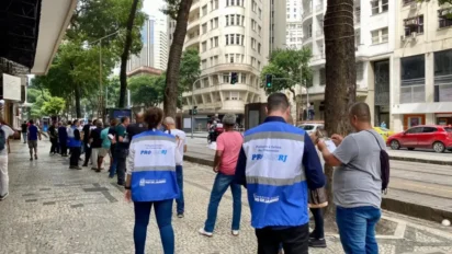 Servidores do Procon/RJ com coletes azuis realizam atendimento ao público em calçada do Centro do Rio de Janeiro, com prédios e pedestres ao fundo. Foto: Divulgação/Procon/RJ
