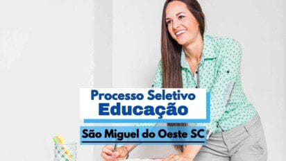 A imagem mostra uma mulher sorridente, de cabelos longos e lisos, vestindo uma camisa verde clara com estampa discreta e calça cinza, inclinada sobre uma mesa enquanto segura uma caneta. À esquerda, há um porta-canetas com itens coloridos. Sobreposta à imagem, há uma faixa com os dizeres “Processo Seletivo Educação” e São Miguel do Oeste SC, indicando a divulgação de uma seleção pública na área da educação.