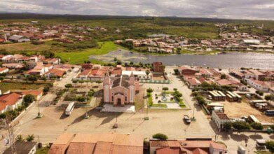 Vista aérea da cidade de Paramoti-CE com destaque para a igreja central, lago ao fundo, casas ao redor e área urbana integrada à paisagem verde. Foto: Divulgação/Aprece - Associação dos Municípios do Estado do Ceará