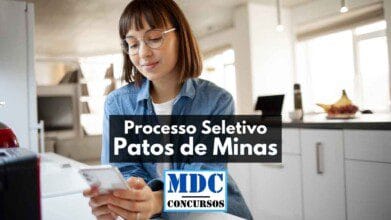 Processos Seletivos 6 Mulher jovem usando óculos e blusa jeans manuseia um celular enquanto está sentada em uma cozinha moderna e iluminada. Na imagem, há sobreposição de texto com os dizeres “Processo Seletivo Patos de Minas” e o logotipo “MDC Concursos”. A cena transmite um momento de concentração, sugerindo que a candidata está realizando inscrição para o processo seletivo por meio de aplicativo.