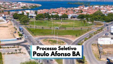 Processos Seletivos 6 Vista aérea de uma grande rotatória arborizada em Paulo Afonso, na Bahia, com ruas asfaltadas ao redor, veículos em circulação e áreas residenciais ao fundo. A imagem destaca o urbanismo organizado da cidade, próxima a um lago visível no horizonte. Em primeiro plano, há uma faixa informativa com os dizeres “Processo Seletivo Paulo Afonso BA”, indicando chamada para seleção pública no município.