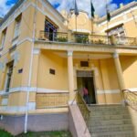 Fachada do prédio da Prefeitura Municipal de Poços de Caldas, em estilo histórico, com escadaria, colunas e bandeiras hasteadas.