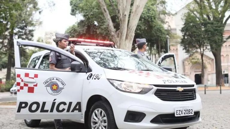 Viatura da Polícia Militar de São Paulo estacionada em via pública com dois policiais fardados ao lado e sirene ligada. Foto: Divulgação/PMSP