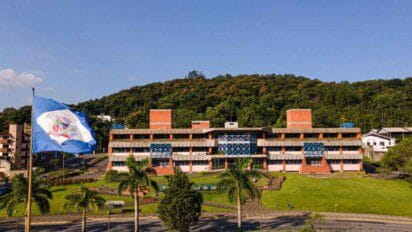 Vista frontal da sede da Prefeitura de Joinville (SC), com bandeira da cidade à esquerda e área arborizada ao fundo. Foto: Divulgação/Prefeitura de Prefeitura Joinville-SC