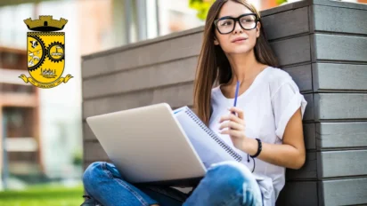 Mulher sentada ao ar livre usando notebook e caderno, em ambiente urbano, com o brasão do município de Agrolândia ao lado, representando estudo e concurso público. Foto: diana.grytsku/Freepik