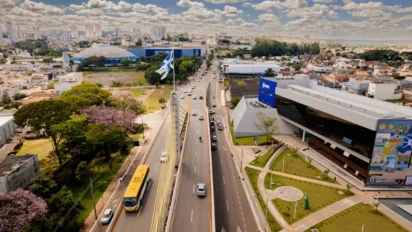 Vista aérea de avenida movimentada em Anápolis com prédios públicos, tráfego de veículos, áreas verdes e bandeira do município ao centro. Foto: Divulgação/Prefeitura de Anápolis-GO