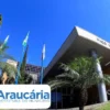 Fachada da Prefeitura de Araucária/PR com bandeiras hasteadas, palmeiras e céu azul, com identificação do município na imagem. Foto: Divulgação/Prefeitura de Araucária-PR