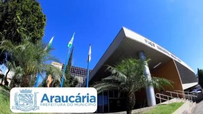 Fachada da Prefeitura de Araucária/PR com bandeiras hasteadas, palmeiras e céu azul, com identificação do município na imagem. Foto: Divulgação/Prefeitura de Araucária-PR