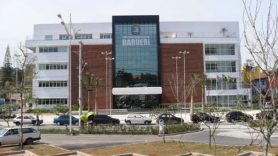 Fachada do prédio da Prefeitura Municipal de Barueri, com edifício moderno, vidro central, nome do município em destaque e veículos estacionados em frente. Foto: Divulgação/Prefeitura de Barueri-SP