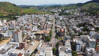 Vista aérea da cidade de Castelo-ES com prédios residenciais, áreas verdes ao fundo e avenida central atravessando a cidade.