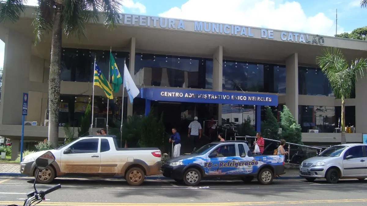 Fachada da Prefeitura Municipal de Catalão com entrada principal, bandeiras hasteadas e pessoas circulando em frente ao prédio.