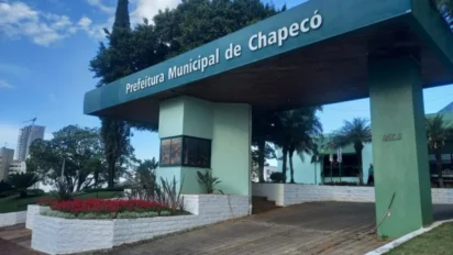 Fachada da Prefeitura Municipal de Chapecó com estrutura verde clara, teto de madeira e letreiro branco, cercada por jardins e árvores sob céu azul. Foto: Divulgação/Prefeitura de Chapecó-SC