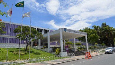 Fachada da Prefeitura de Contagem/MG com bandeiras hasteadas, prédio moderno de cor roxa e área ajardinada em dia ensolarado. Foto: Divulgação/Câmara de Contagem-MG