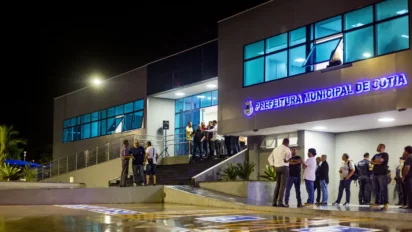 Prédio da Prefeitura Municipal de Cotia iluminado à noite, com pessoas reunidas na entrada e janelas de vidro azuladas. Foto: Divulgação/Prefeitura de Prefeitura de Cotia-SP