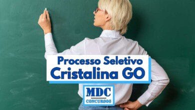 Processos Seletivos 9 Imagem de uma mulher de cabelos loiros curtos e óculos vermelhos, vista de costas, escrevendo em um quadro verde com giz branco, vestindo camisa branca de mangas compridas e calça jeans, com a mão esquerda na cintura e a direita levantada segurando o giz, sobreposta por uma faixa com os dizeres Processo Seletivo Cristalina GO e o logotipo MDC Concursos em destaque abaixo do texto