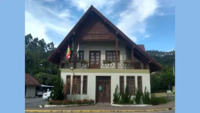 Fachada da Prefeitura Municipal de Doutor Pedrinho, em Santa Catarina. O prédio possui dois pavimentos, com arquitetura em estilo enxaimel, telhado inclinado de madeira e bandeiras hasteadas na sacada frontal.