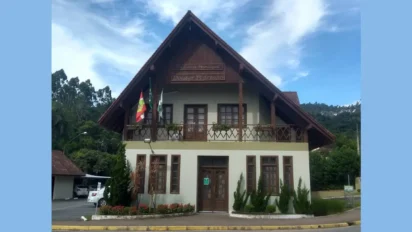 Fachada da Prefeitura Municipal de Doutor Pedrinho, em Santa Catarina. O prédio possui dois pavimentos, com arquitetura em estilo enxaimel, telhado inclinado de madeira e bandeiras hasteadas na sacada frontal.