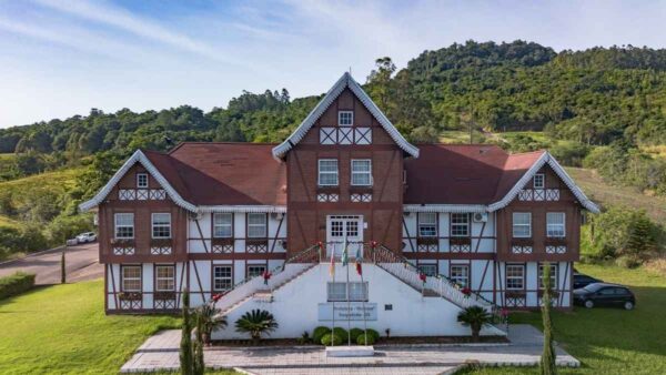 Concurso Forquetinha RS divulga homologação das inscrições para 11 vagas 4 Fachada da Prefeitura de Forquetinha/RS com arquitetura em estilo enxaimel, escadaria central, bandeiras e vegetação ao redor. Foto: Divulgação/Prefeitura de Forquetinha-RS