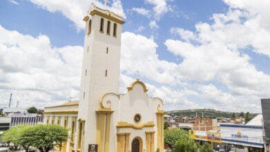 Processos Seletivos 4 Igreja Matriz de Sant’Ana em Gravatá-PE com torre alta, fachada branca e detalhes em amarelo, sob céu azul com nuvens. Foto: Bruno Lima - MTUR/Wikipédia