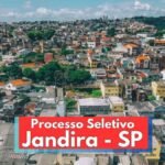 Imagem panorâmica da cidade de Jandira, em São Paulo, com destaque para uma área urbana densamente ocupada, composta por diversas casas e prédios coloridos. A paisagem mostra ruas arborizadas, construções de diferentes tamanhos e estilos, além de um céu azul com nuvens. Na parte inferior da imagem, há uma faixa vermelha com os dizeres “Processo Seletivo Jandira - SP” em destaque.