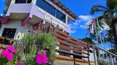 Prédio da Prefeitura Municipal de Jarinu/SP com jardim florido em primeiro plano e bandeiras hasteadas ao lado. Foto: Divulgação/Prefeitura de Jarinu-SP