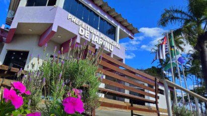 Prédio da Prefeitura Municipal de Jarinu/SP com jardim florido em primeiro plano e bandeiras hasteadas ao lado. Foto: Divulgação/Prefeitura de Jarinu-SP