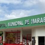Fachada do Hospital Municipal de Marabá, no estado do Pará, com destaque para a placa verde com letras metálicas que identificam a instituição. À direita, há o logotipo da Prefeitura de Marabá com a frase "Um Governo por Todos". O céu está parcialmente nublado e parte da vegetação e portão de entrada do hospital também são visíveis na imagem.