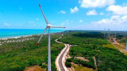 Aeroportas de energia eólica próximas ao litoral com estrada cercada por vegetação e mar ao fundo. Foto: Divulgação/Prefeitura de Mataraca-PB