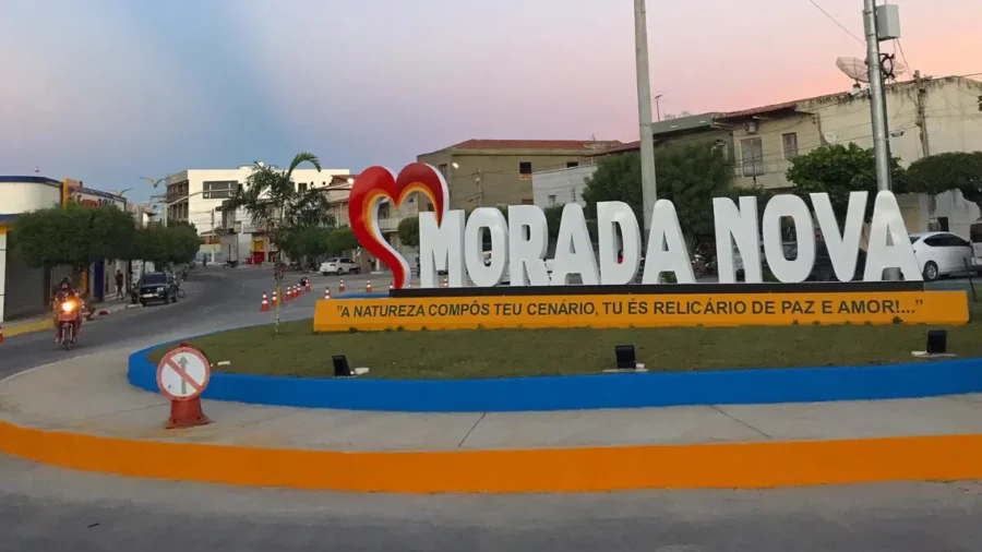 Letreiro monumental com o nome da cidade de Morada Nova em uma rotatória urbana, exibindo um coração estilizado e uma frase de boas-vindas sobre base amarela.