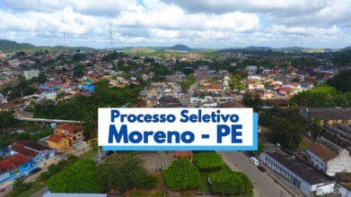 Vista panorâmica da cidade de Moreno, em Pernambuco, com destaque para a área urbana composta por casas coloridas, vegetação densa e relevo com morros ao fundo. No centro da imagem, há uma faixa com os dizeres “Processo Seletivo Moreno - PE” em letras azuis, indicando a abertura de vagas pela prefeitura local. O céu está parcialmente nublado, com iluminação natural suave.