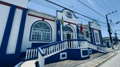 Fachada da Prefeitura de Penha, em Santa Catarina, com prédio histórico nas cores azul e branco, escadaria frontal, bandeiras hasteadas e rua ao redor em dia ensolarado. Foto: Divulgação/Prefeitura de Penha-SC