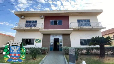 Fachada do Paço Municipal de Populina, um prédio de dois pavimentos em tons de bege e bordô com o brasão da cidade sobreposto no canto inferior esquerdo. O edifício possui janelas de vidro, sacadas com guarda-corpo metálico e um pequeno jardim frontal com arbustos e uma palmeira. Foto: Divulgação/Google Maps (Prefeitura de Populina-SP)