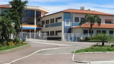 Fachada da Prefeitura de Rio das Ostras com prédio administrativo, portões brancos, jardim com palmeiras e calçada em primeiro plano sob céu azul. Foto: Divulgação/Prefeitura de Rio das Ostras-RJ