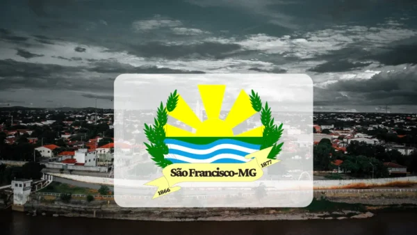 Brasão de São Francisco, Minas Gerais, centralizado sobre uma vista aérea da cidade em tons de cinza. O emblema contém um sol amarelo, ondas azuis e ramos verdes, acompanhado de uma faixa amarela com o nome do município e os anos 1866 e 1877. Foto: Divulgação/Prefeitura de São Francisco-MG