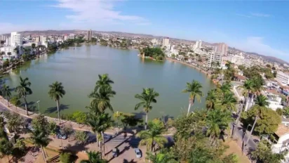 Vista aérea da Lagoa Paulino em Sete Lagoas/MG, com palmeiras ao redor, vias urbanas e prédios ao fundo em dia ensolarado. Foto: Luiz Claudio Alvarenga/Wikipédia