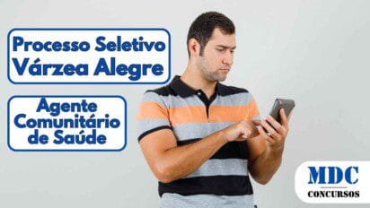 Homem jovem de pele clara, usando camisa polo listrada em preto, cinza e laranja, segurando um smartphone e tocando na tela com expressão de concentração - Prefeitura de Várzea Alegre (CE) abre Seleção para Agente Comunitário de Saúde