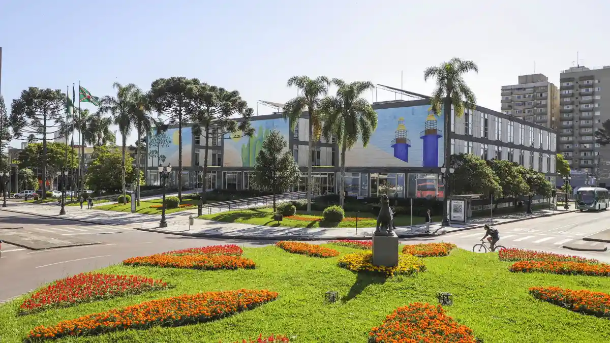 Fachada da Prefeitura Municipal de Curitiba com jardins floridos em destaque, ilustrando a abertura do processo seletivo Curitiba para o cargo de engenheiro civil