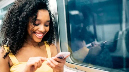 Mulher sorridente usando celular enquanto viaja de transporte público. Foto: HelloDavidPradoPerucha/Freepik
