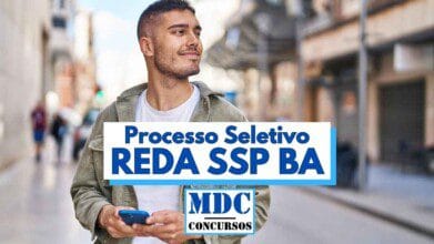 Homem jovem de barba rala e cabelo curto sorri enquanto caminha por uma rua urbana segurando um celular azul, vestindo camiseta branca e jaqueta verde clara com capuz, em frente a uma paisagem urbana desfocada com pedestres e prédios ao fundo; sobre a imagem há um destaque em texto azul com a frase "Processo Seletivo REDA SSP BA" e o logotipo "MDC Concursos" abaixo