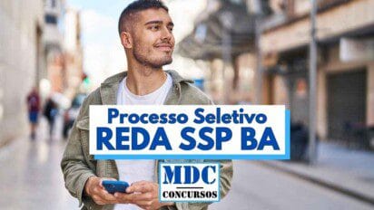 Homem jovem de barba rala e cabelo curto sorri enquanto caminha por uma rua urbana segurando um celular azul, vestindo camiseta branca e jaqueta verde clara com capuz, em frente a uma paisagem urbana desfocada com pedestres e prédios ao fundo; sobre a imagem há um destaque em texto azul com a frase "Processo Seletivo REDA SSP BA" e o logotipo "MDC Concursos" abaixo