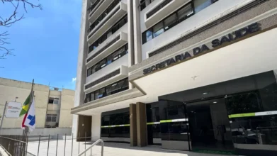 Fachada de prédio da Secretaria da Saúde com entrada principal envidraçada e bandeiras hasteadas ao lado. Foto: Divulgação/Silviane Mannrich/Ascom SES