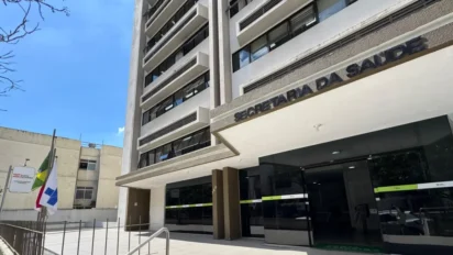 Fachada de prédio da Secretaria da Saúde com entrada principal envidraçada e bandeiras hasteadas ao lado. Foto: Divulgação/Silviane Mannrich/Ascom SES