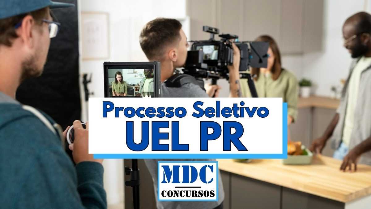 Imagem de bastidores de uma gravação em estúdio com uma equipe de filmagem registrando duas pessoas em uma cozinha moderna, enquanto um cinegrafista ajusta a câmera principal e outro profissional segura um monitor externo exibindo a cena gravada; em destaque no centro da imagem está um banner com os dizeres “Processo Seletivo UEL PR” e da “MDC Concursos” na parte inferior