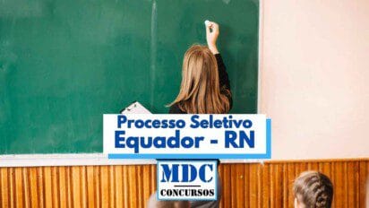 Imagem de uma professora de costas escrevendo em um quadro verde com giz, em uma sala de aula. Ela segura uma prancheta na mão esquerda e está usando roupas escuras. Em primeiro plano, aparecem parcialmente duas crianças sentadas. Na parte central da imagem há uma faixa com os dizeres "Processo Seletivo Equador - RN" e o logotipo "MDC Concursos" em destaque.
